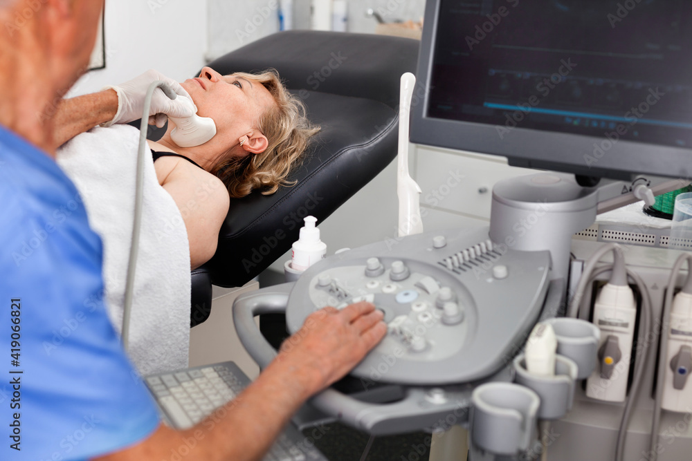 Naklejka premium Elderly diligent efficient friendly man sonographer using ultrasonography machine checking female patient in hospital diagnostic room