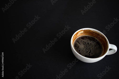 White cup of aromatic coffee on a black background. The cup is on the saucer. White cup of aromatic freshly ground arabica coffee on a black background. Top view. with copy space.