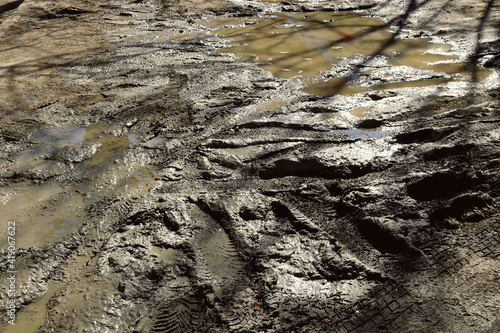 Fotografi muddy water puddle on the street with uneven mud texture with wheel tracks from