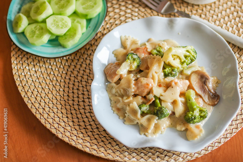 Farfalle pasta in cheese sauce with chicken on a wooden table, top view close-up.