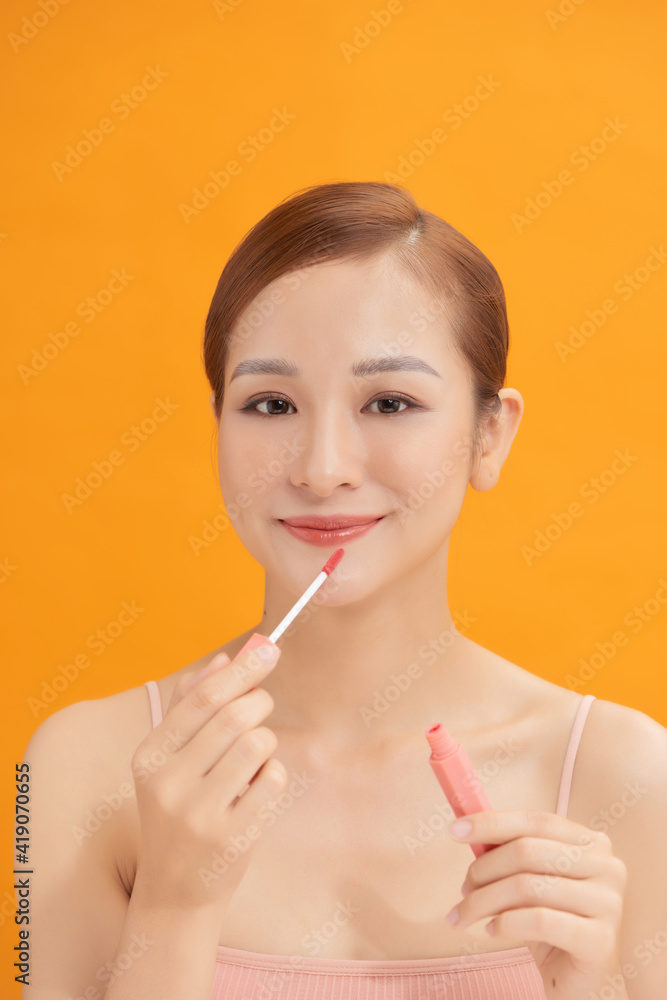 Beauty portrait of a pretty young topless woman wearing makeup isolated over yellow background, applying lip gloss Beauty portrait of a pretty young topless woman wearing makeup isolated over yellow background, applying lip gloss