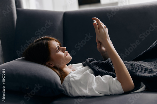 woman under the covers on the sofa and mobile phone in hand