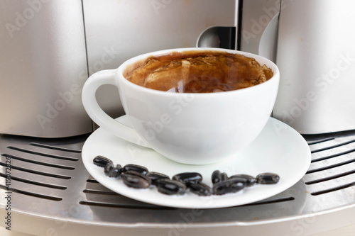 Brewing fresh coffee from your espresso machine. Budget coffee maker. White cup decorated with coffee beans