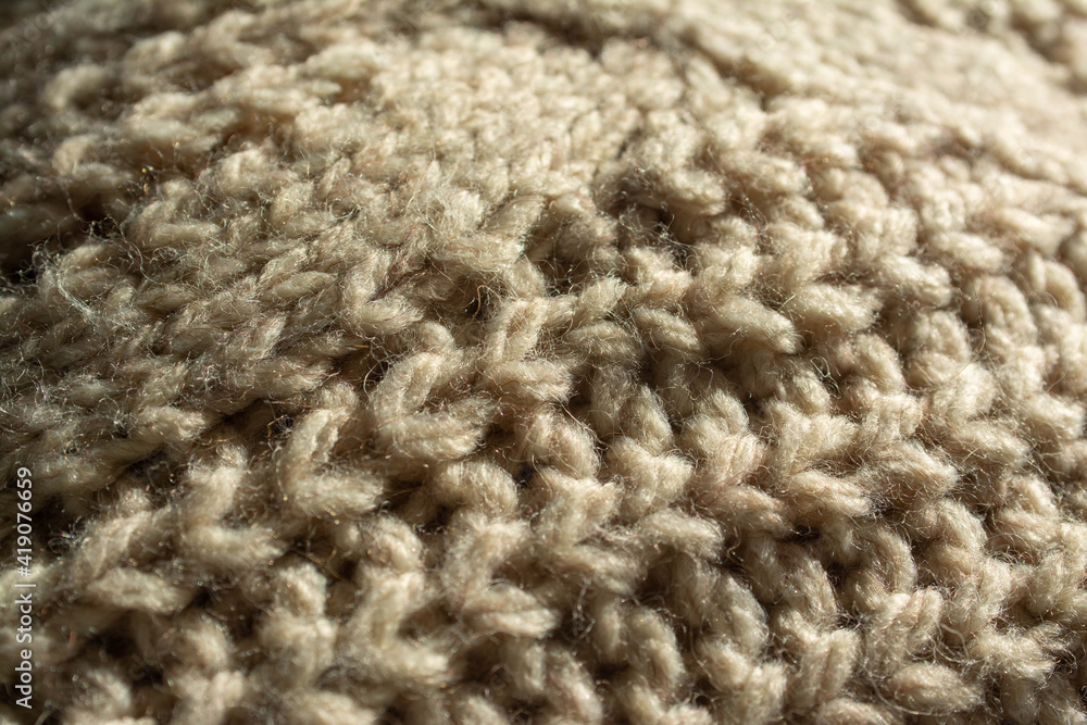 Diagonal closeup of a large knitted jumper, with central twist, English knit. Beige, natural colour. Diagonal closeup of a large knitted jumper, with central twist, English knit. Beige, natural colour.