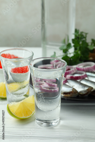 Shots of vodka and tasty snacks on white wooden background
