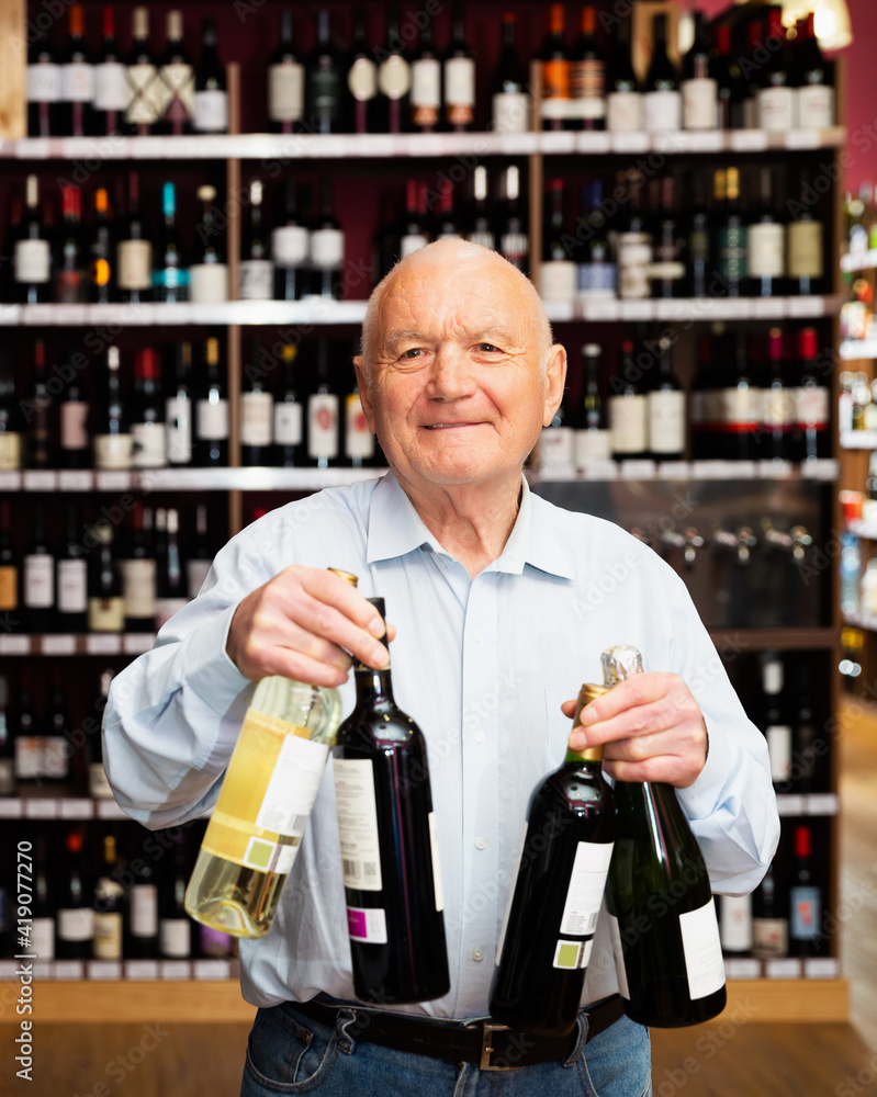 Portrait of joyful elderly man with bottles of wine at the liquor store