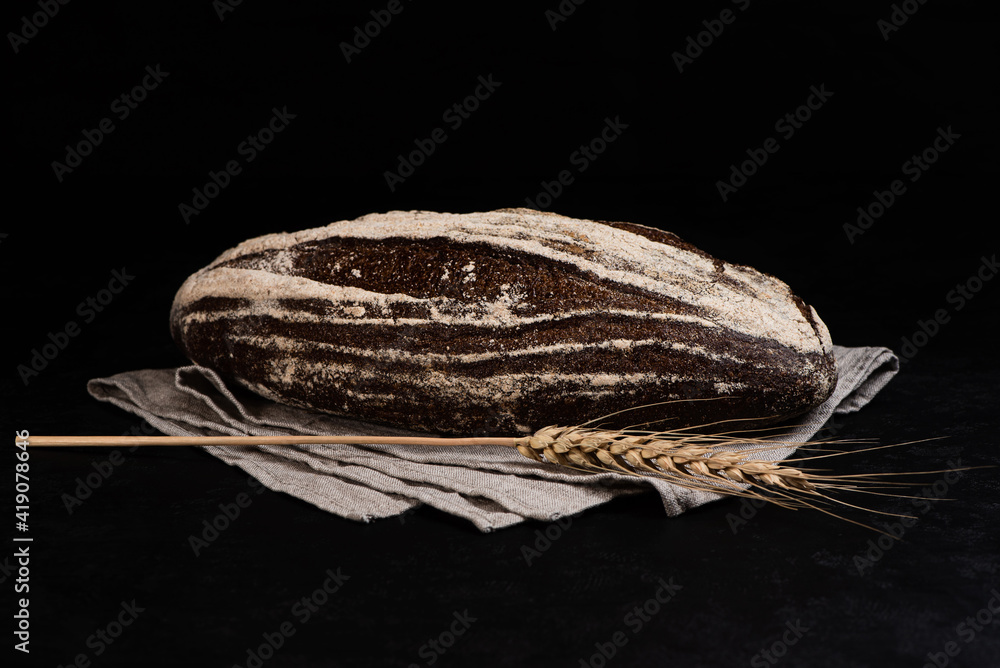 Homemade sourdough rye bread with caraway seeds and spikelet on gray textile napkin on dark background. Copy space.