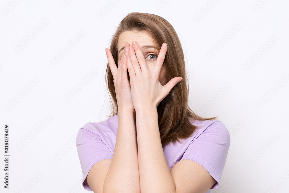 close up scared girl hiding face in palms hands and peering out with one eye between her fingers, trembling fear close up scared girl hiding face in palms hands and peering out with one eye between her fingers, trembling fear