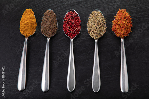 Spoons with different spices and seasonings on black slate