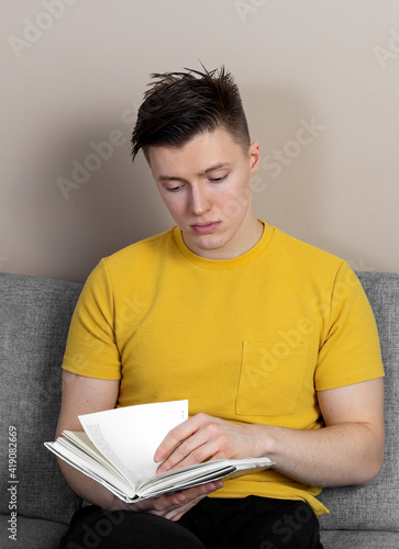 A young man is sitting on the sofa and reading a book. High quality photo