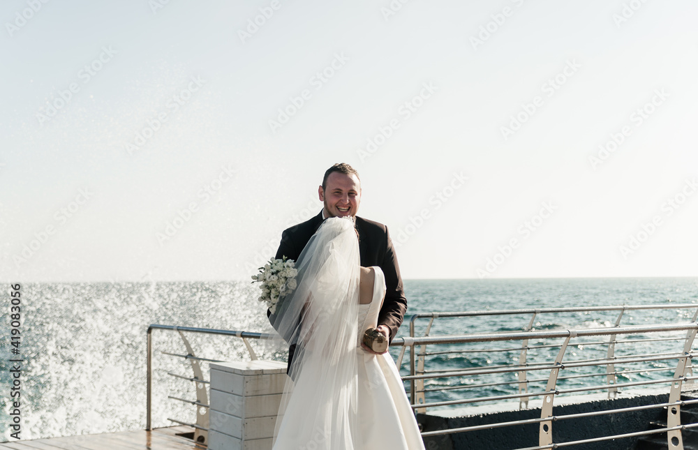 beautiful couple groom and bride are hugging on the pier against the backdrop of the sea and splashing waves. couple walks near the sea. happy newlyweds at the sea. cute wedding couple beautiful couple groom and bride are hugging on the pier against the backdrop of the sea and splashing waves. couple walks near the sea. happy newlyweds at the sea. cute wedding couple