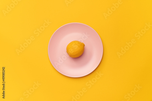 Fresh lemon on a pink plate on a yellow background. The lemon in the center of the frame. Minimalism. Minimal cooking concept