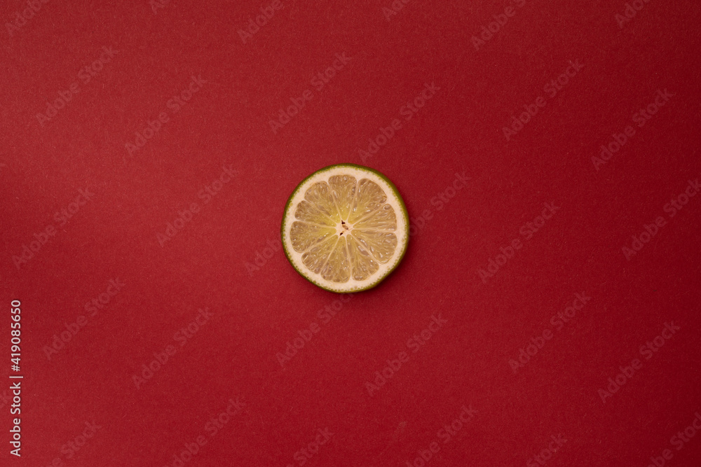 Slice of a lime on a deep red background. The lime in the center of the frame. Minimalism