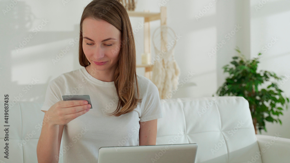Young businesswoman at home makes a purchase on the Internet. Woman buyer with laptop using credit card purchasing things on internet shop sitting on couch at home. Young businesswoman at home makes a purchase on the Internet. Woman buyer with laptop using credit card purchasing things on internet shop sitting on couch at home.