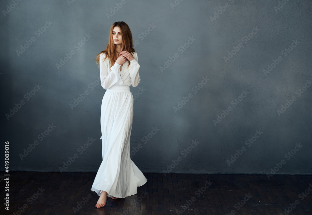 Red-haired Woman in a white dress in full growth on a gray background indoors Red-haired Woman in a white dress in full growth on a gray background indoors