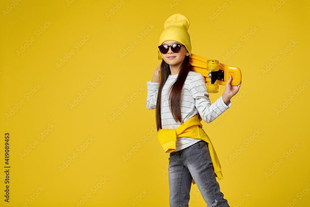 cool hipster little child girl in sunglasses posing with yellow skateboard on studio background. copy space