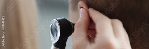 Otorhinolaryngologist pulling ear with his hand and looking at it with otoscope closeup