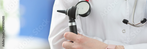 Otorhinolaryngologist holding otoscope in his hands in clinic closeup