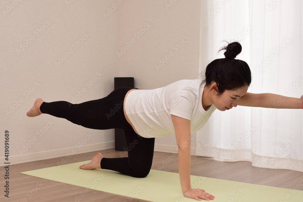 Naklejka premium A young pregnant woman is doing fitness at home. It is important to exercise during pregnancy.