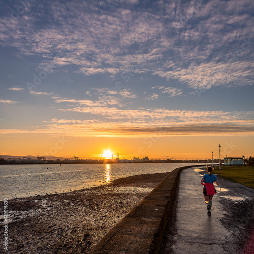 Photography unrecognizable woman running on the coast of Dublin harbor at sunset
