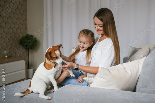 Young mom with her daughter playing with Jack Russell Terrier dog. Family and pet at home.