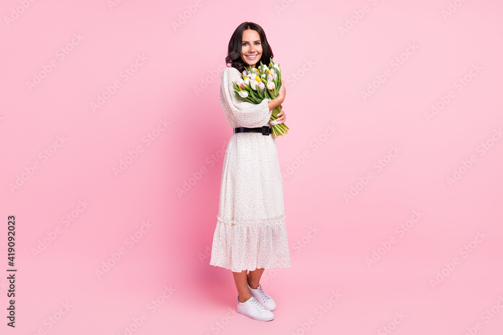 Full body photo of charming attractive young woman hold hands spring flowers isolated on pastel pink color background Full body photo of charming attractive young woman hold hands spring flowers isolated on pastel pink color background