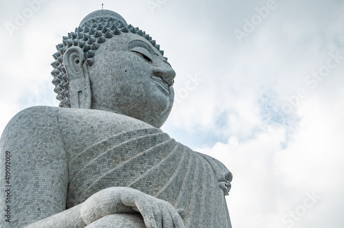 The giant statue of the Big Buddha in Phuket  made of stone  is turned three-quarters in a sitting position with a hand resting on the armrest. One of the main attractions of the resort