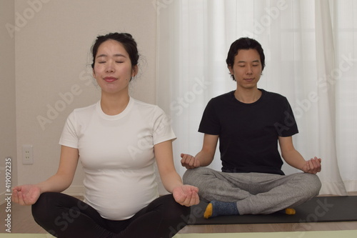 A young pregnant woman is doing fitness at home. The couple are sitting and meditating. It is important to exercise during pregnancy.