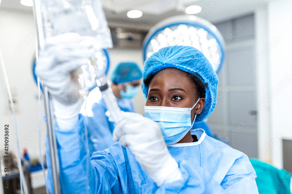 African american female Doctor in the operating room putting drugs through an IV - surgery concepts African american female Doctor in the operating room putting drugs through an IV - surgery concepts