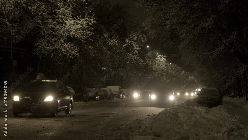 Cars passing by at night in winter with trees and cars covered with snow Cars passing by at night in winter with trees and cars covered with snow