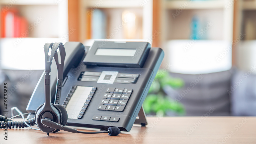 Close up soft focus on headset with telephone devices at office desk for customer service support.VOIP headset for customer service support (call center) concept. Close up soft focus on headset with telephone devices at office desk for customer service support.VOIP headset for customer service support (call center) concept.