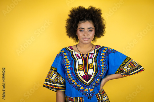 African american woman wearing african clothing over yellow background with a happy face standing and smiling with a confident smile showing teeth