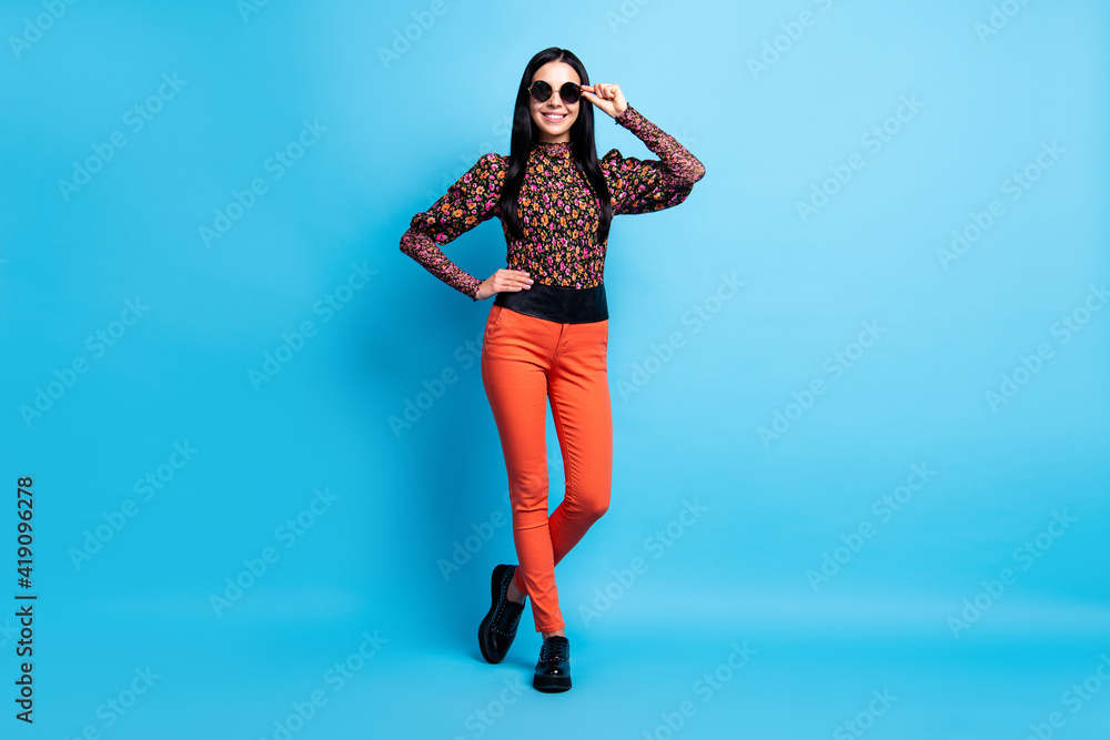 Photo of confident lady posing look camera wear retro specs flower print shirt pants boots isolated blue color background Photo of confident lady posing look camera wear retro specs flower print shirt pants boots isolated blue color background