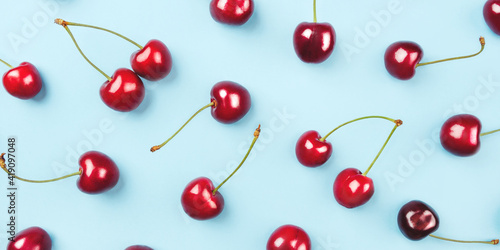 Bright pattern of ripe cherries on a blue background. Flat lay, top view.