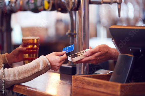 Close Up Of Female Customer In Bar Making Contactless Payment With Card For Drinks To Male Bartender