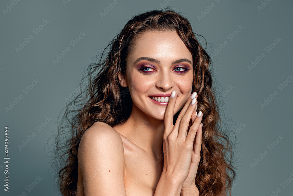 A beautiful young woman with a stunning healthy smile of long hair poses. Smooth teeth. Shiny natural curly hair. Evening make-up. A beautiful young woman with a stunning healthy smile of long hair poses. Smooth teeth. Shiny natural curly hair. Evening make-up.