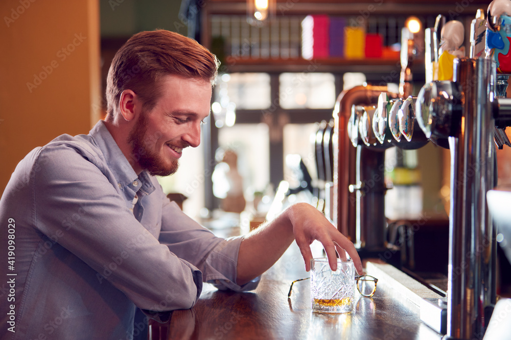 Close Up Of Smiling Man Sitting At Pub Bar Enjoying Glass Of Whisky
