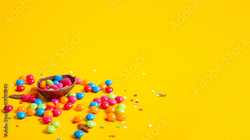 Banner. Chocolate Easter eggs with colored candies on a yellow background.