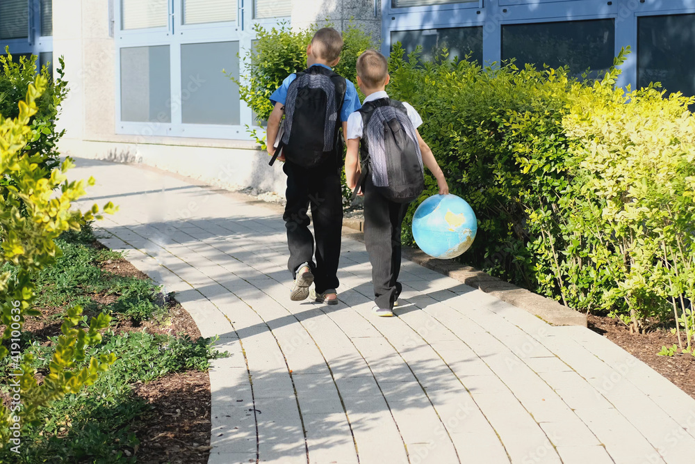 two boys, schoolchildren in black school uniforms with backpacks go to ...