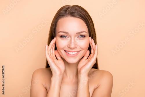Portrait of attractive cheerful girl touching face using natural facial cream isolated over beige pastel color background