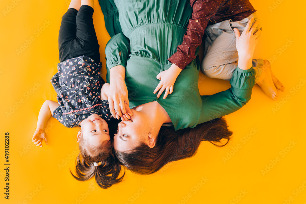 Obraz premium Happy mom with children lie on yellow background. Spending time with children.