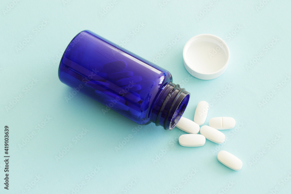 spilled white pills on blue background and blue medicine bottle spilled white pills on blue background and blue medicine bottle