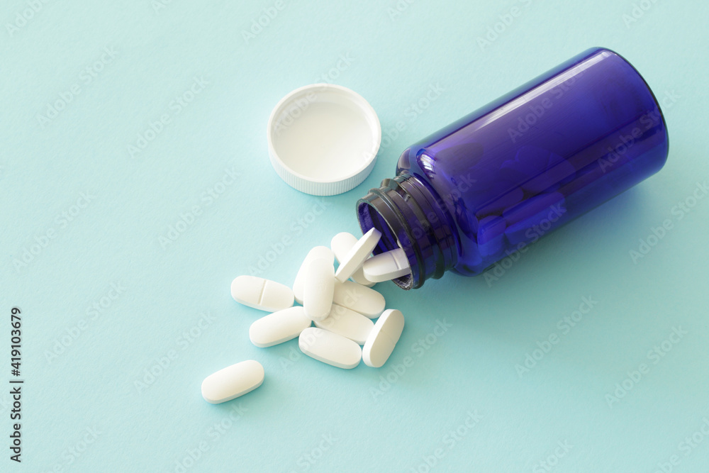 spilled white pills on blue background and blue medicine bottle spilled white pills on blue background and blue medicine bottle