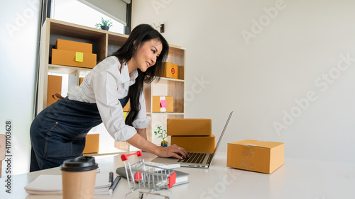 Small Business Startup Freelance SME Entrepreneurs Beautiful Asian Young Women Working at Home with Box, Smartphone, Laptop on the Table with Online Sales, Marketing, Packaging, SME Shipping, Ecommerc photo