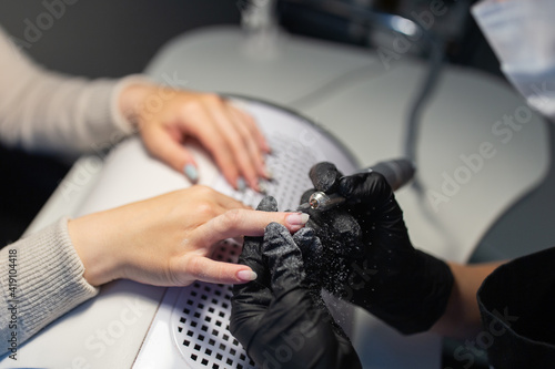 Crop master doing manicure to female client. Faceless master in black gloves removing shellac nail polish from nails of faceless woman with nail drill machine