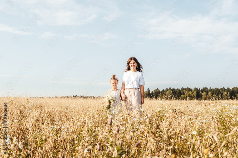 Beautiful young mother and her daughter in field. White clothes, freedom concept. Copy space, front view. Beautiful young mother and her daughter in field. White clothes, freedom concept. Copy space, front view.