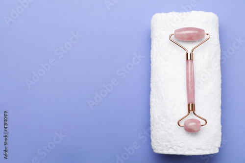 Natural face roller and towel on lilac background, top view. Space for text © New Africa