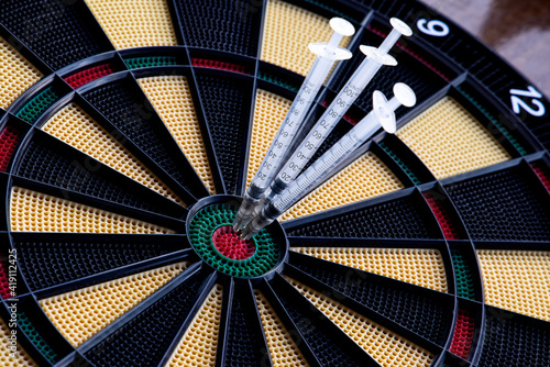 A closeup of dartboard with syringe in the red center, bulls eye. A concept for corona virus pandemic and mass vaccination in the world. Stop the spread of covid 19