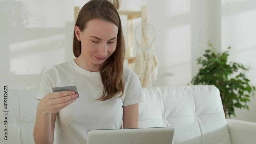 Young businesswoman at home makes a purchase on the Internet. Woman buyer with laptop using credit card purchasing things on internet shop sitting on couch at home. Young businesswoman at home makes a purchase on the Internet. Woman buyer with laptop using credit card purchasing things on internet shop sitting on couch at home.