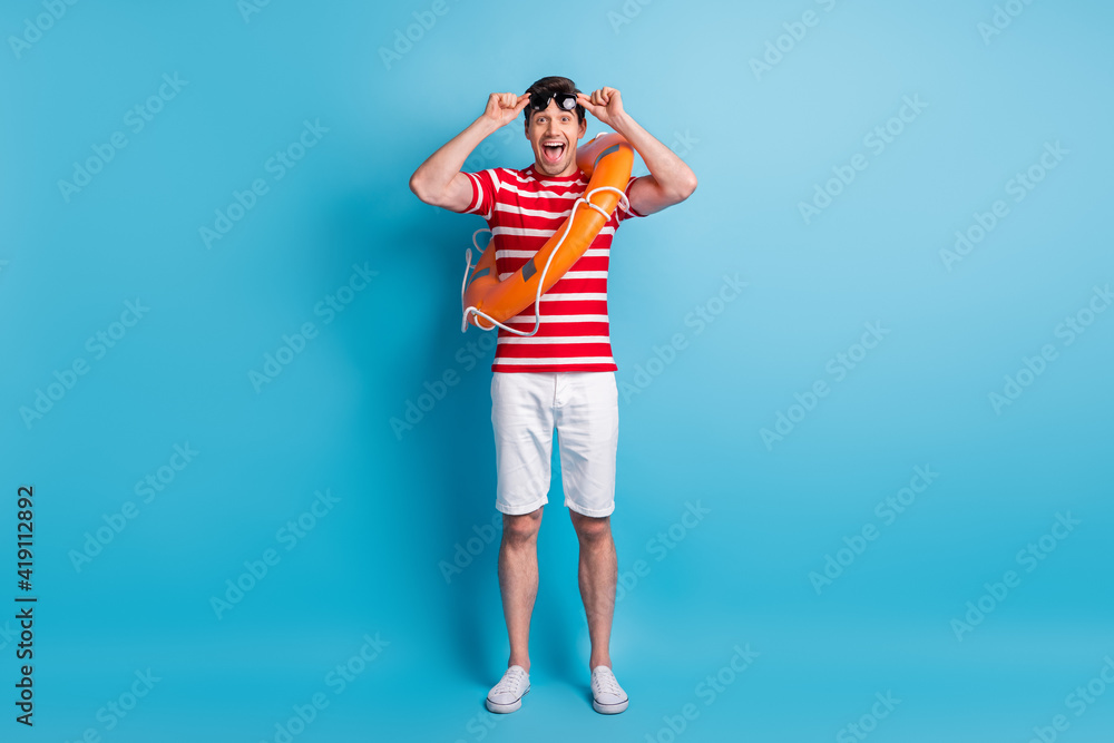 Full length body photo man wearing orange circle sunglass relaxing near sea isolated on bright blue color background Full length body photo man wearing orange circle sunglass relaxing near sea isolated on bright blue color background